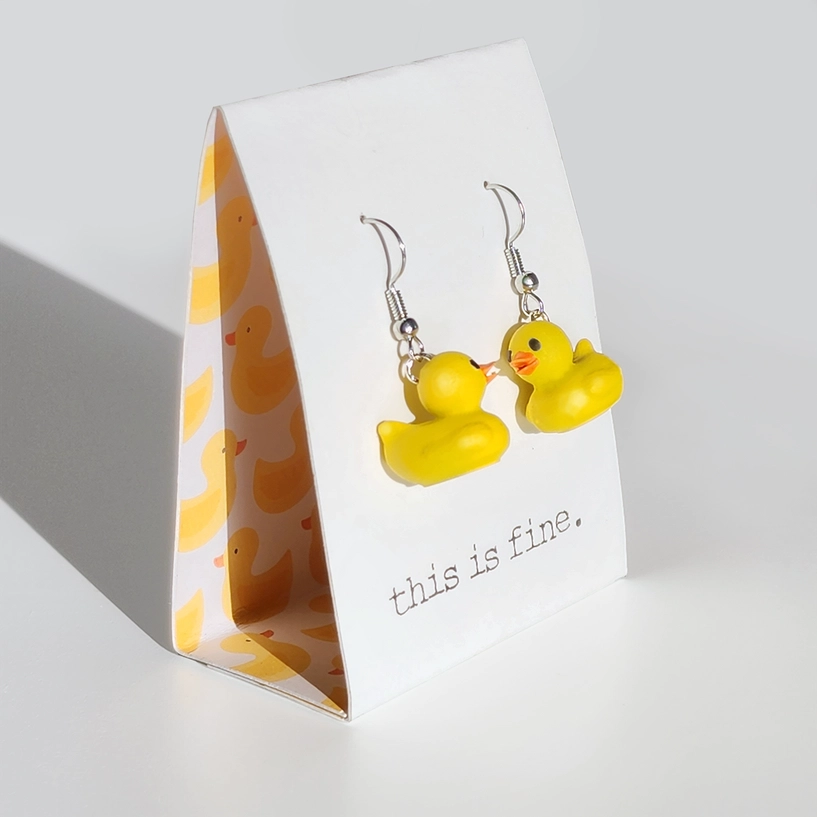 Yellow duck-shaped earrings on a stand with 'this is fine' text