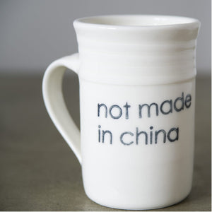 white porcelain cup with stamp like print that says "not made in Canada"