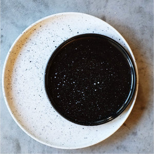 a small black plate with white specks on top of a white large plate with black specks
