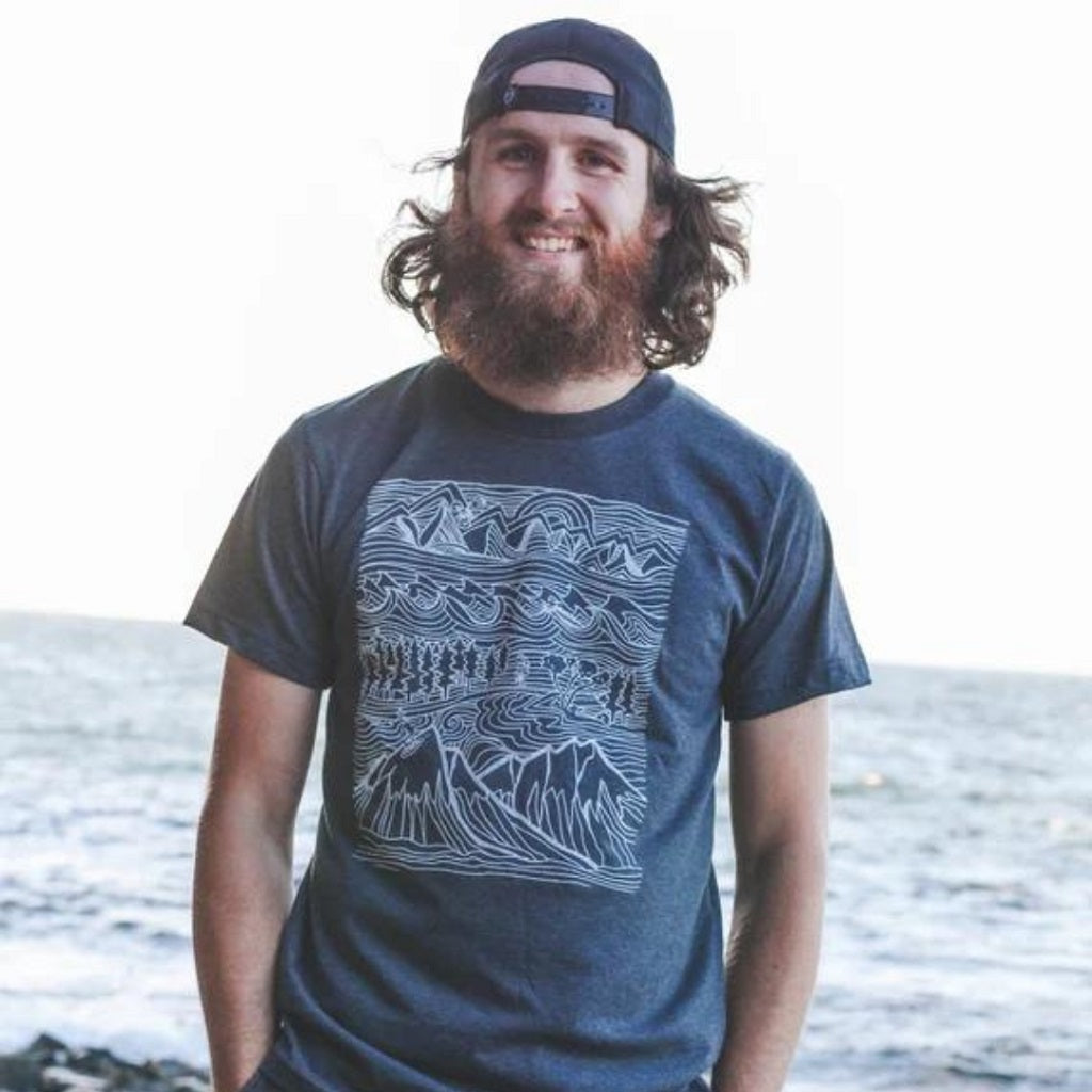 scruffy bearded man wearing a baseball hat backwards & t shirt with a mountain print in white