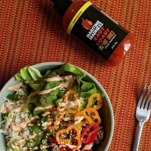 Load image into Gallery viewer, table with a plate of salad and a fork with a bottle labeled Hot Sauce in orange
