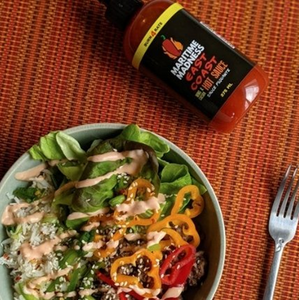 table with a plate of salad and a fork with a bottle labeled Hot Sauce in orange