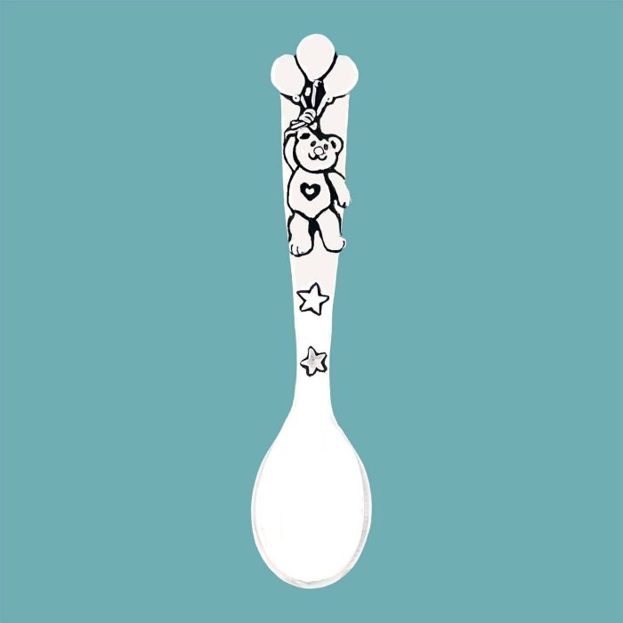 A white baby spoon featuring a black line-art illustration of a teddy bear holding balloons on the handle, set against a solid teal background.