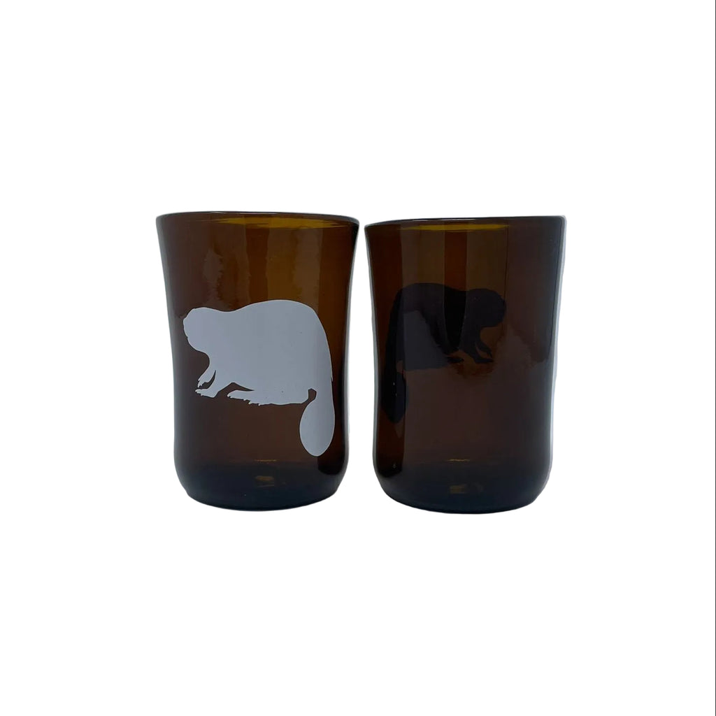 Two recycled beer bottle amber glasses with white beaver silhouettes, standing side by side on a light gray background.