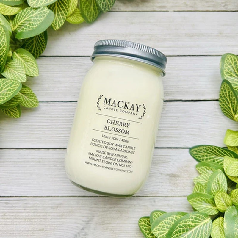 Mackay Candle Company cherry blossom candle jar on a wooden surface with green leaves.