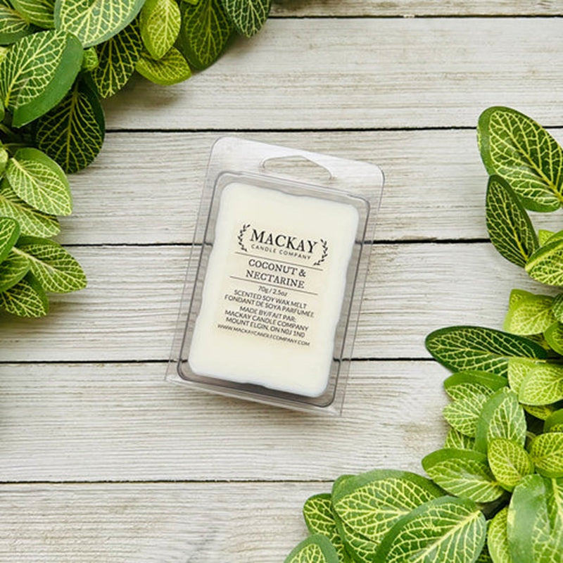 Mackay Coconut & Nectarine wax melt packaging on a wooden surface with green leaves.