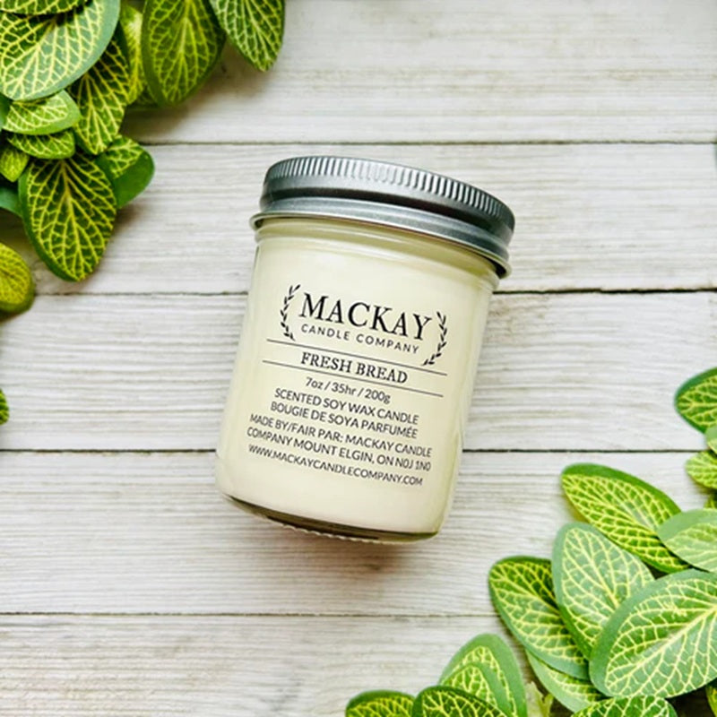 Mackay Candle Company candle with 'Fresh Bread' scent on a wooden surface with green leaves.