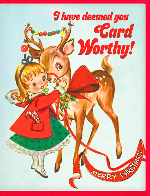 Vintage Christmas greeting card illustration featuring a young girl in a red coat and green skirt hugging a brown deer with antlers. The card has a pale blue background with red text reading 'I have deemed you Card Worthy!' and 'MERRY CHRISTMAS!' on a red border.