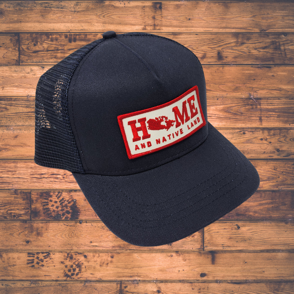 Black trucker cap with a red and white 'Home and Native Land' patch on a wooden surface