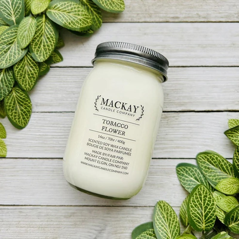 Mackay Candle Company candle in a jar on a wooden surface with green leaves.