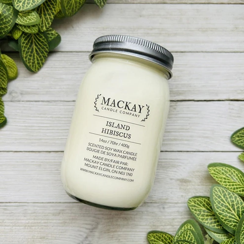 Mackay Candle Company candle in a jar on a wooden surface with green leaves.