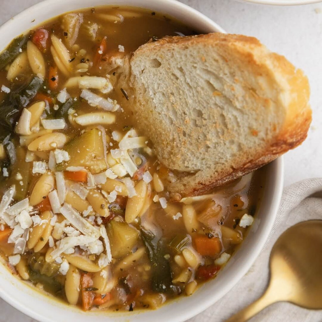 Lemon Chicken Orzo soup with bread in a white bowl on a light background