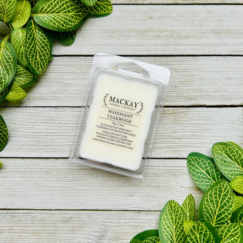 Mackay Candle Company wax melt packaging on a wooden surface with green leaves.