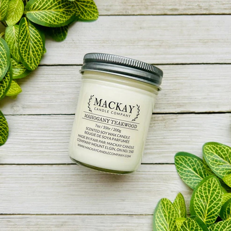 Jar of Mackay Candle Company candle on a wooden surface with green leaves