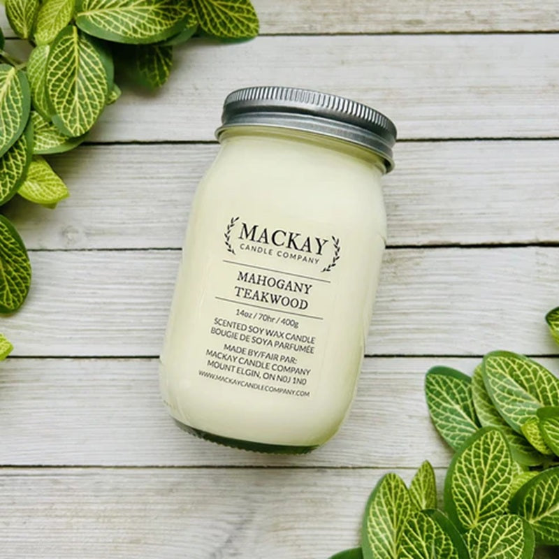 Mackay Candle Company candle in a mason jar on a wooden surface with green leaves.