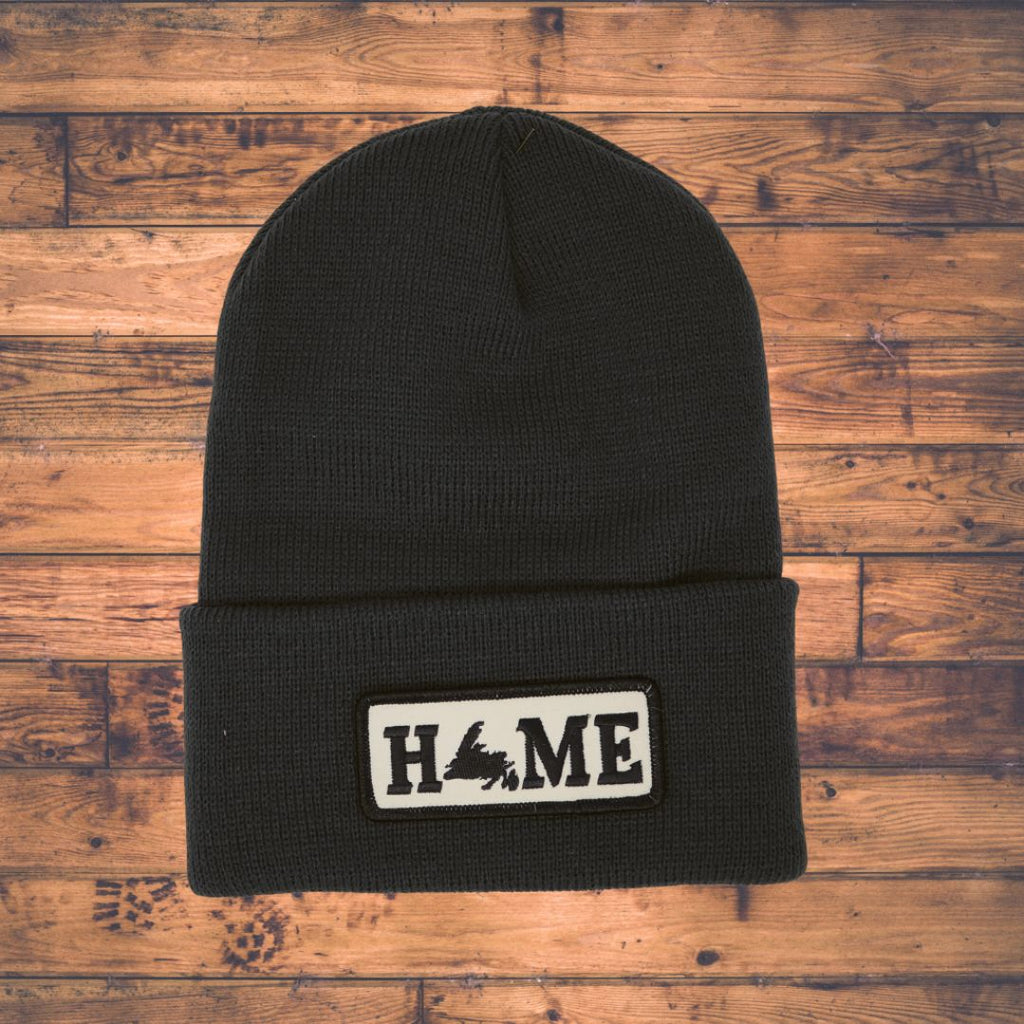 Black beanie with 'HOME' patch on a wooden surface