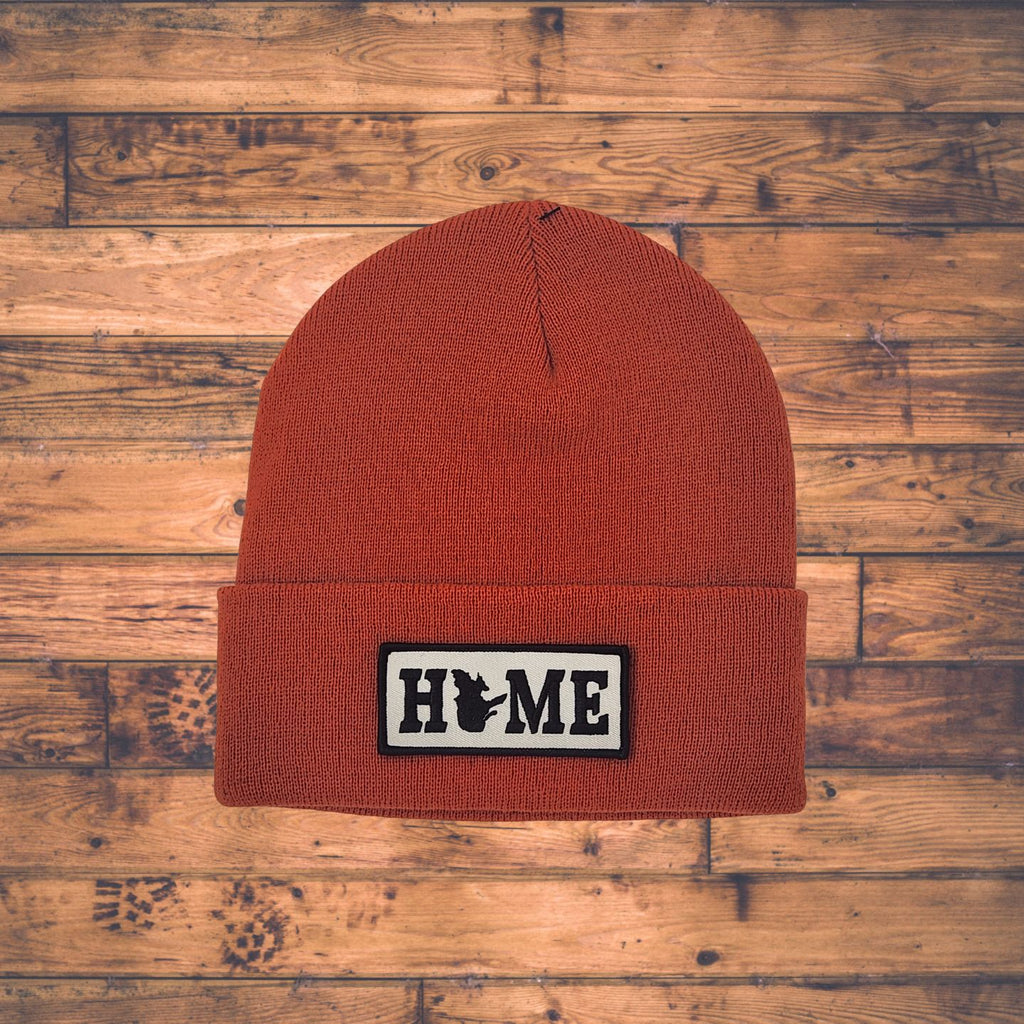 Brown beanie with Quebec 'HOME' patch on a wooden surface