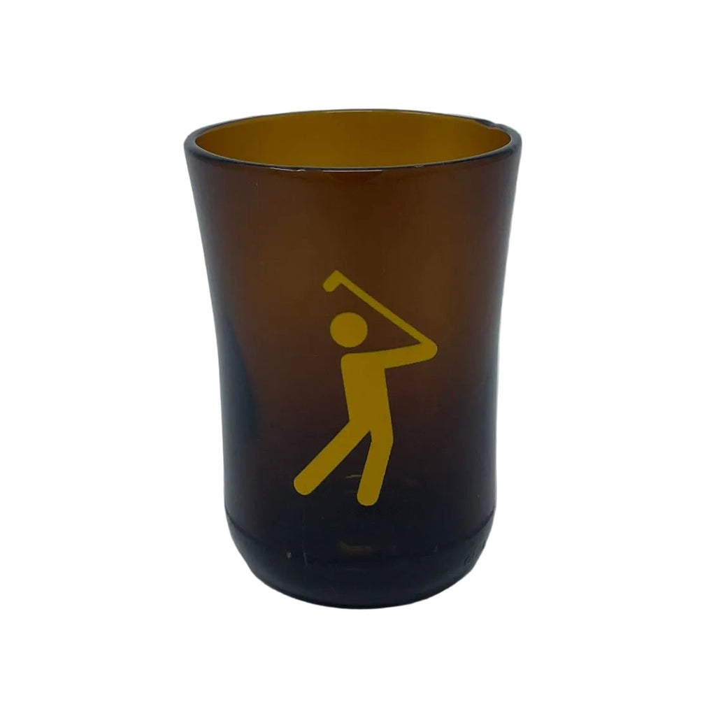 An amber brown translucent shot glass featuring a yellow graphic of a golfer, set against a plain light gray background.