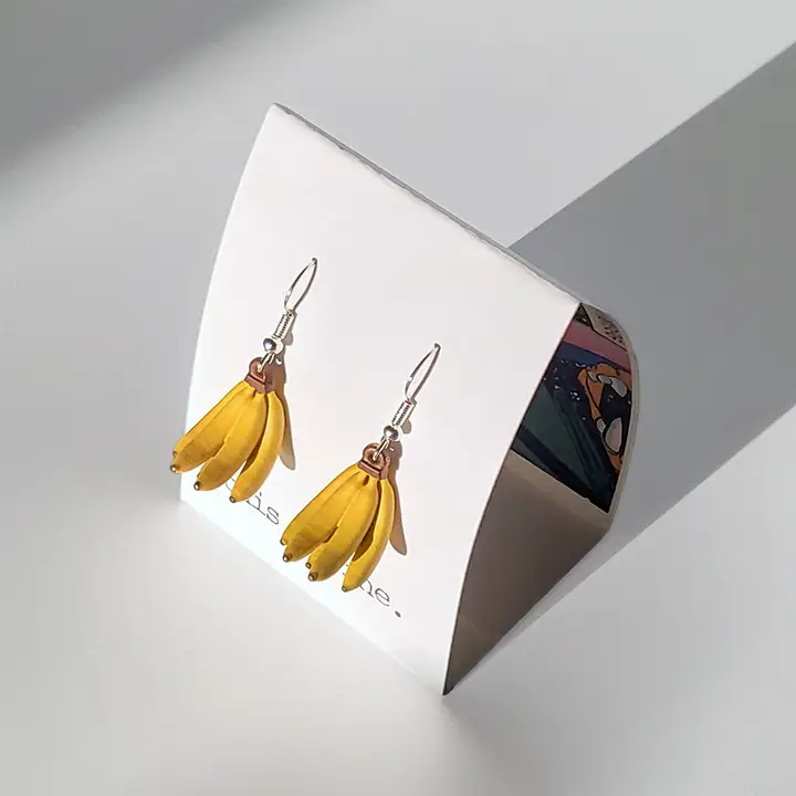 Banana-shaped earrings on a stand with a gray background