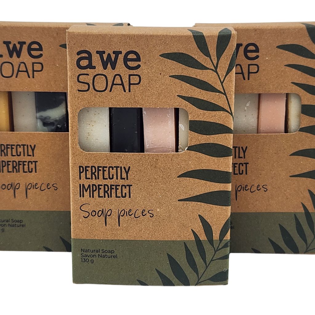 3 brown & green boxes with black print and a cut out window filled with soap ends