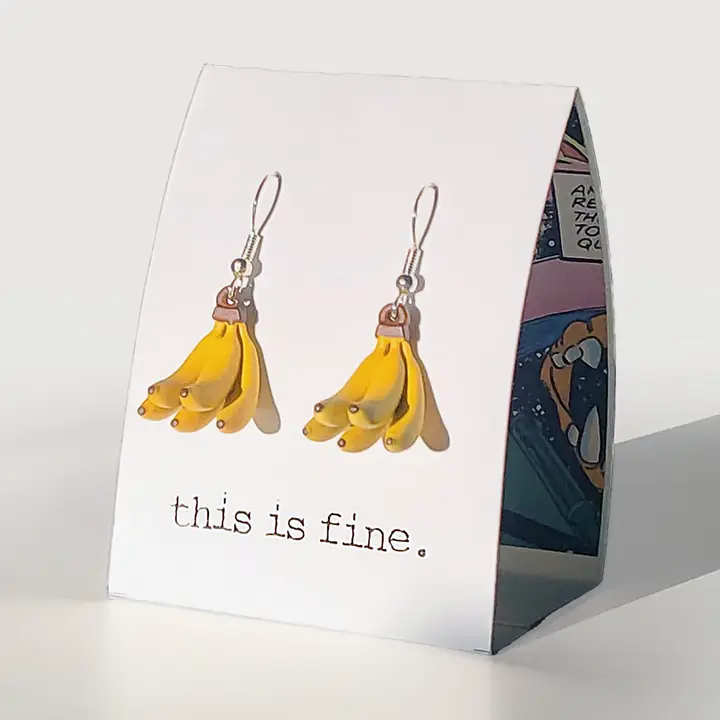 Banana-shaped earrings on a card with 'this is fine' text, displayed against a white background.