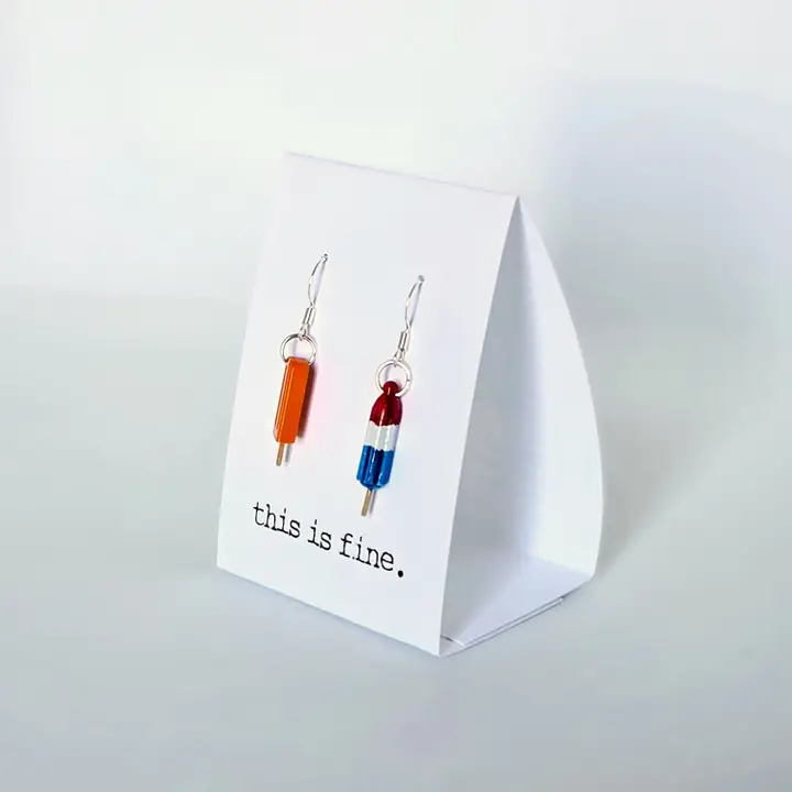 Pair of earrings on a 'this is fine' card against a white background