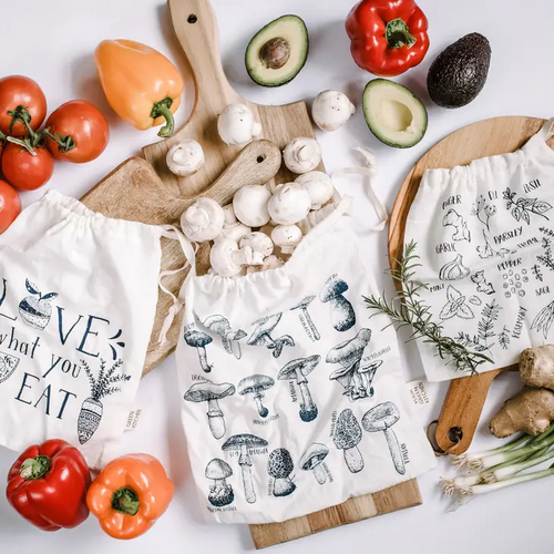 three bags with black print (mushroom, love what you eat & herbs) on a counter with fresh veggies