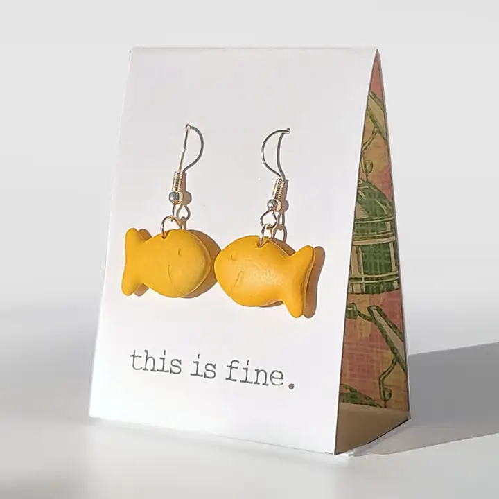 Yellow fish-shaped earrings on a card with 'this is fine.' text, against a white background.