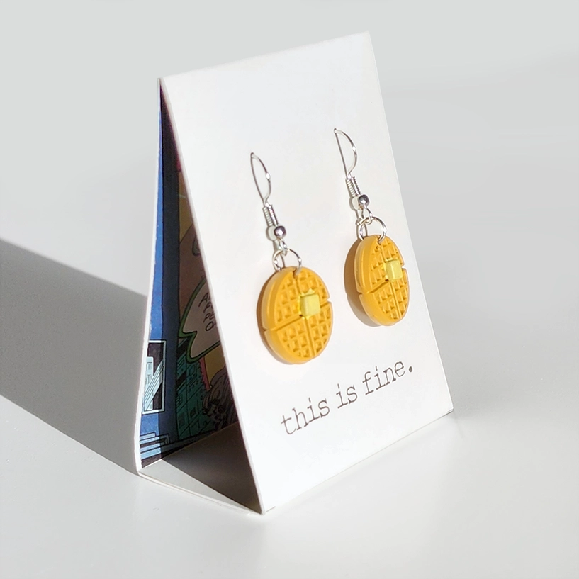 Yellow earrings on a card with 'this is fine' text, displayed on a white surface.