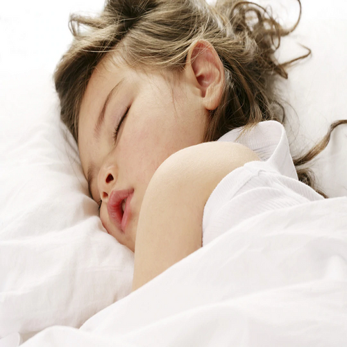 child with brown tasseled hair sleeping with duvet