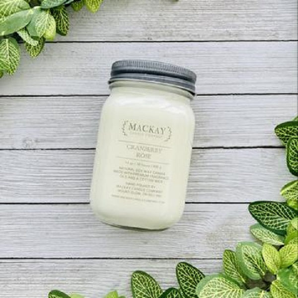 Mason jar filled with white candle laying on a white washed planks with a bit of greenery