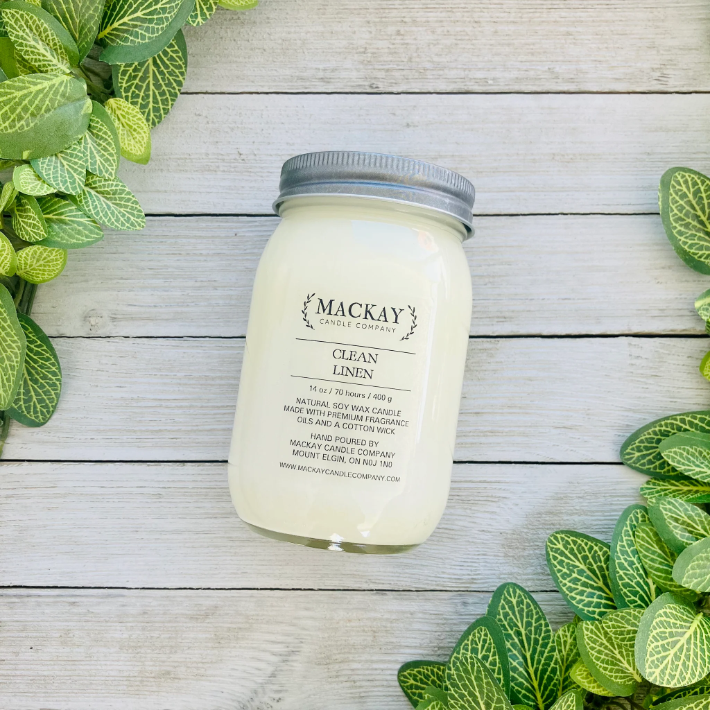 Mason jar filled with white candle, pewter lid and clear label with MacKay and other info