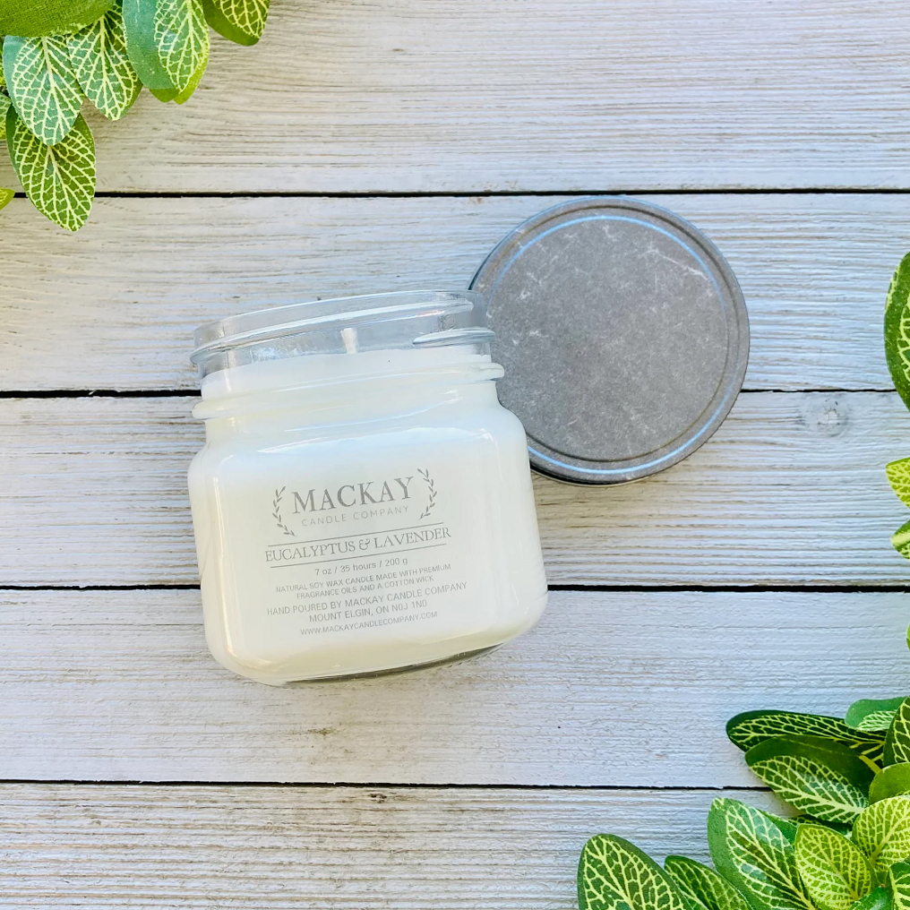 Mason jar filled with white candle, pewter lid and clear label with MacKay and other info