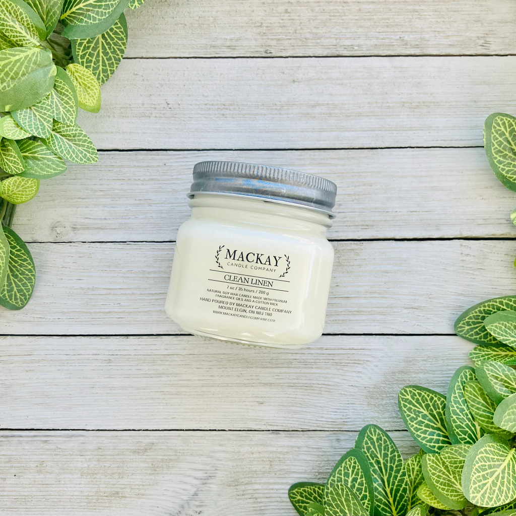 Mason jar filled with white candle, pewter lid and clear label with MacKay and other info
